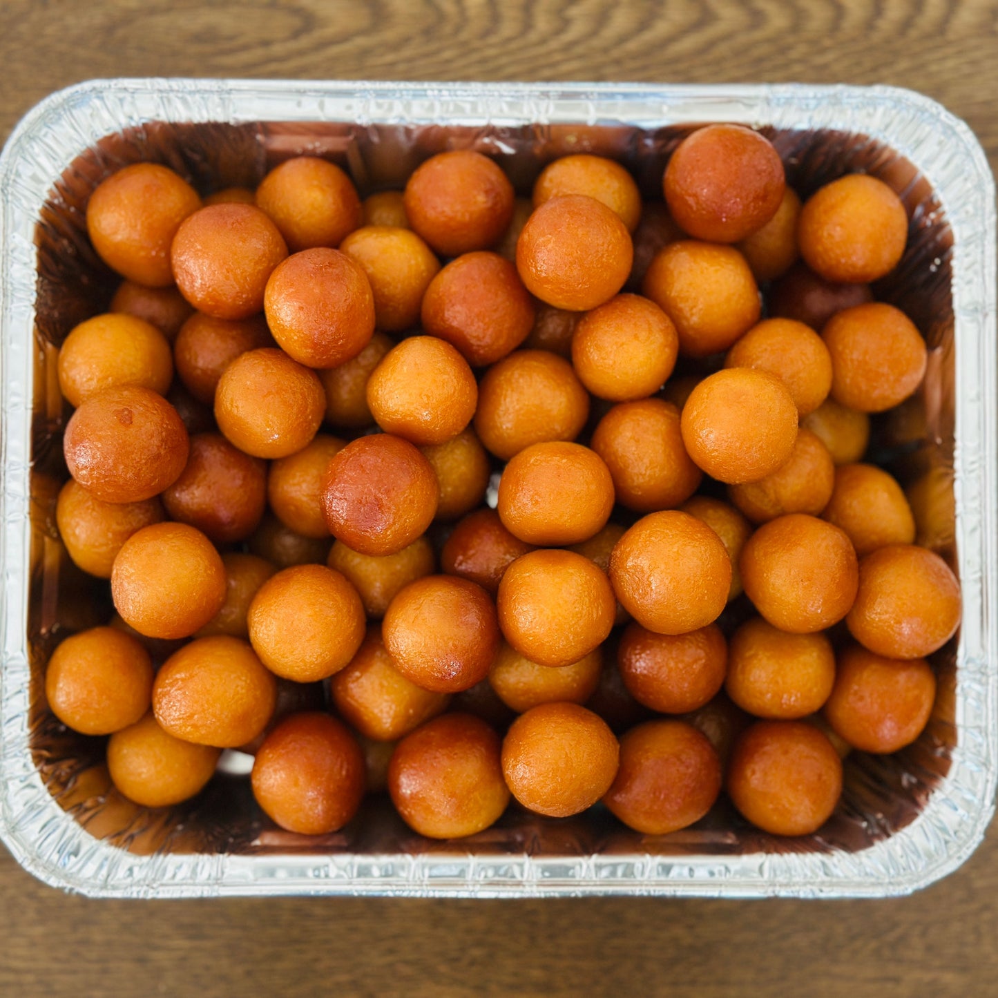 Warm, syrup-soaked Gulab Jamuns elegantly arranged on a polished silver serving tray, showcasing Royal Ruby's premium Indian mithai.