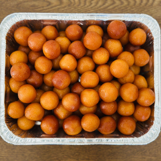 Warm, syrup-soaked Gulab Jamuns elegantly arranged on a polished silver serving tray, showcasing Royal Ruby's premium Indian mithai.