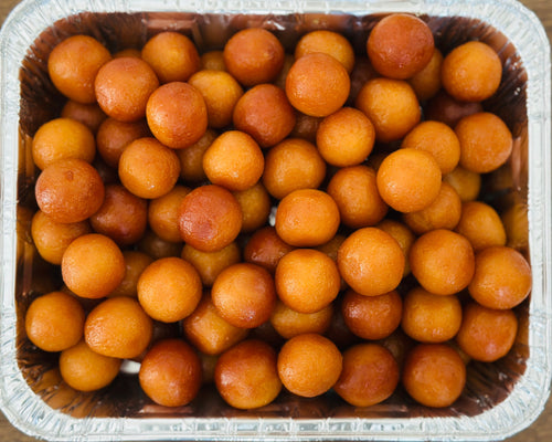 Warm, syrup-soaked Gulab Jamuns elegantly arranged on a polished silver serving tray, showcasing Royal Ruby's premium Indian mithai.