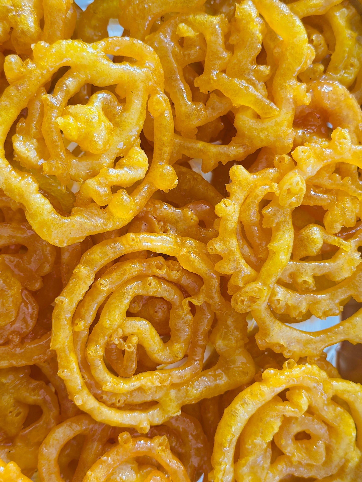 Crisp, golden Jalebis glistening with cardamom syrup, elegantly presented on a tiered silver cake stand alongside a vintage teacup.
