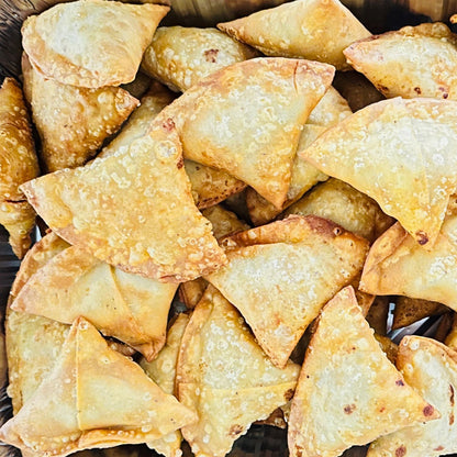 A plate featuring three large, golden-brown handmade samosas from Royal Ruby. Two classic potato and peas samosas sit next to a Shahi Paneer samosa that is broken open to reveal a rich, creamy paneer filling inside.